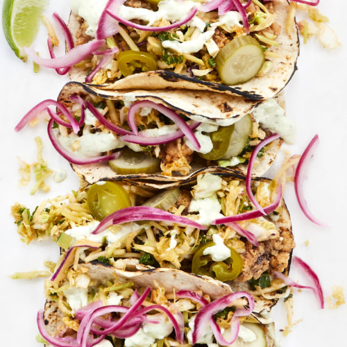 fried chicken tacos with tangy slaw, pickles, jalapeños, cilantro and crema