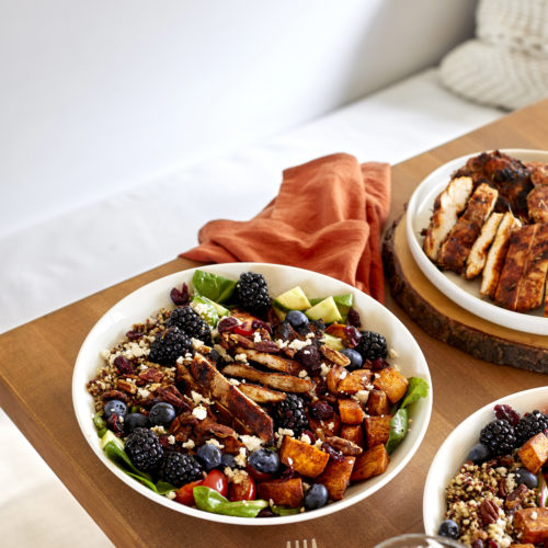 spicy chicken grain bowl filled with spicy chicken, coconut quinoa, cinnamon sweet potatoes, cucumbers, pecans, blackberries, cherry tomatoes and a balsamic glaze