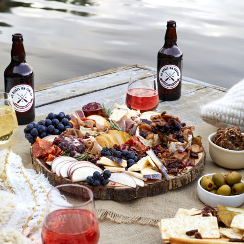 fall charcuterie board with meat, cheese, brie, merlot, spiked cider, no boats on sunday cider, olives, figs, pecans, grapes, pears and pomegranates.