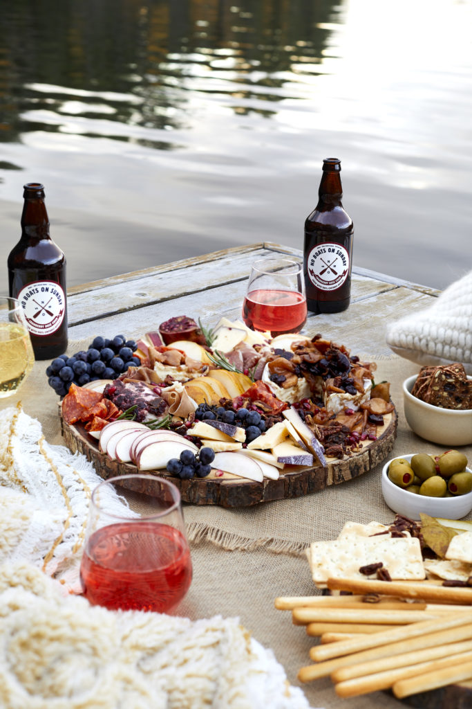 fall charcuterie board with meat, cheese, brie, merlot, spiked cider, no boats on sunday cider, olives, figs, pecans, grapes, pears and pomegranates. 